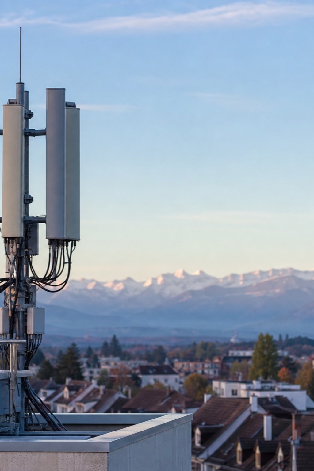 Kompakte Mobilfunk-Antennen auf einem Dach vor klarem Schweizer Himmel mit Alpen und Wohnhäusern in der Distanz
