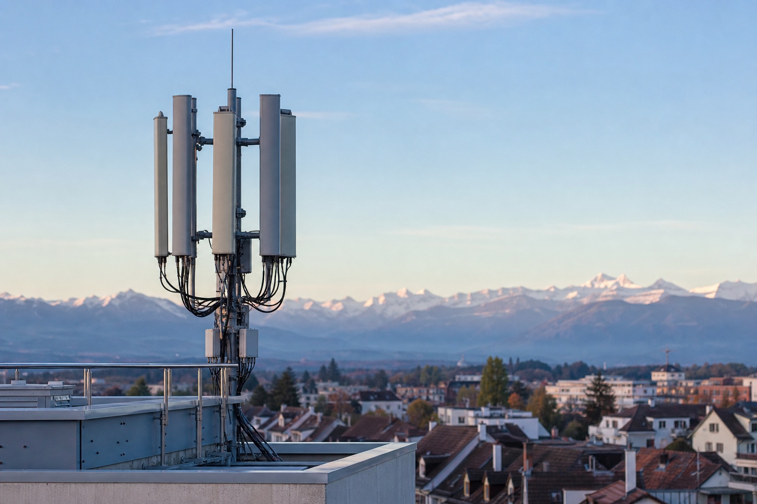 Kompakte Mobilfunk-Antennen auf einem Dach vor klarem Schweizer Himmel mit Alpen und Wohnhäusern in der Distanz
