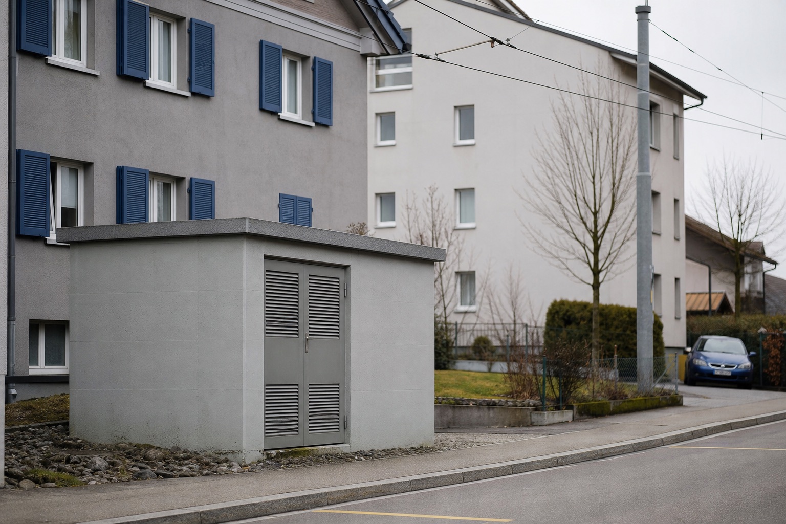 Ruhige Quartierstrasse mit kleiner Ortsnetz-Transformatorstation, Mehrfamilienhaus-Fassaden und Niederspannungsleitung